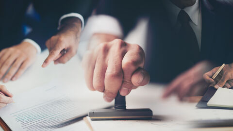 Nahaufnahme einer Hand edie mit genehmigtem Stempel auf dem Dokument am Schreibtisch stempelt 