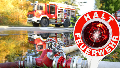 Feuerwehr bei einem Einsatz, Feuerwehrauto im Hintergrund, vorne Feuerwehrschlauch und Kelle "Halt Feuerwehr"