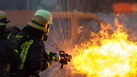 Feuerwehrmann oder -frau löscht ein Feuer mit einem Wasserschlauch