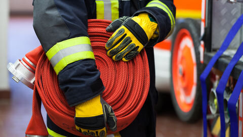 Feuerwehrmann oder - frau hält Feuerwehrschlauch Feuerwehrmann oder - frau hält Feuerwehrschlauch