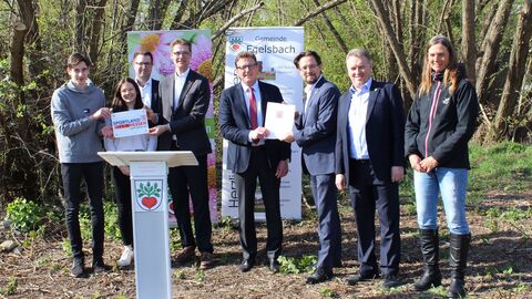 Staatssekretär Stefan Sauer (Mitte) steht gemeinsam mit den Beteiligten vor Bäumen und übergibt den Förderbescheid.