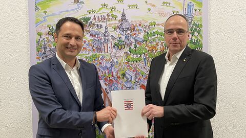 Innenminister Peter Beuth überreicht Bürgermeister Joachim Reimann den Förderbescheid, beide lächeln