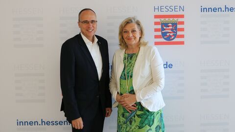 Minister Peter Beuth und Landesbeauftragte Margarete Ziegler-Raschdorf vor Fotowand mit Logo des Hessischen Innenministeriums.