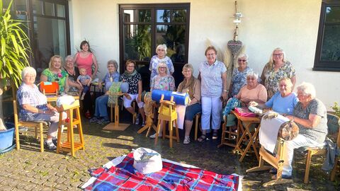 Die Frauen der Klöppelgruppe sitzen gemeinsam im Halbkreis an ihrem Handwerk.
