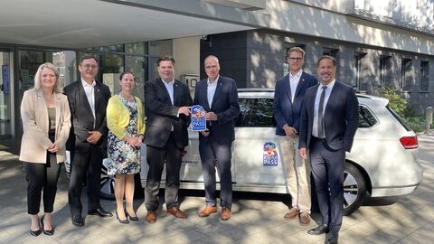 Innenminister Beuth gemeinsam mit Beteiligten der Stadt vor einem Gebäude. Sie stehen vor einem Auto und der Innenminister überreicht das Sicherheitssiegel.