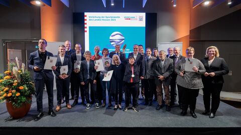 Die Preisträgerinnen und Preisträger der Sportplakette stehen nebeneinander zum Gruppenfoto aufgestellt und halten ihre Ehrungen in Händen.