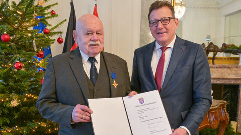 Staatssekretär Sauer gemeinsam mit Hand-Jürgen Litzinger. Die beiden halten gemeinsam die Urkunde in Händen und stehen vor einem Weihnachtsbaum.