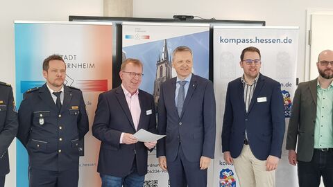 Staatssekretär Martin Rößler händigt Urkunde an Bürgermeister Ralf Möller aus. Im Hintegrund sind einige Aufsteller zur KOMPASS zu sehen.