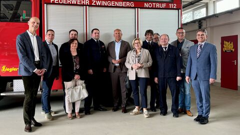 Innenminister Roman Poseck, Bürgermeister Holger Habich, Stadtverordnetenvorsteher Andreas Kovar, Stadtbrandinspektor Reiner Schellhaas, Landtagsabgeordneter Alexander Bauer und Landtagsabgeordnete Birgit Heitland stehen gemeinsam vor einem Feuerwehrfahrzeug in einer Halle.