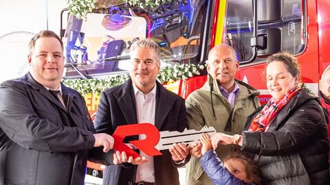 Innenminister Poseck mit weiteren Personen vor einem Feuerwehrfahrzeug. Er übergibt symbolisch einen großen Schlüssel.