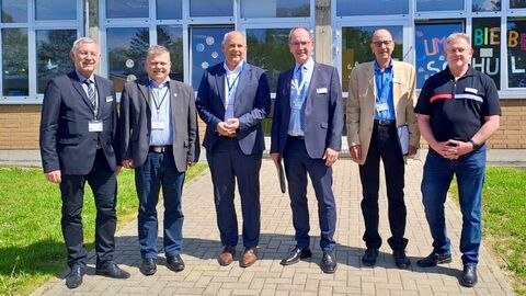 Innenminister Roman Poseck, Bürgermeister Thomas Groll und Regierungspräsident Christoph Ullrich mit weiteren Vertretern des Regierungspräsidiums stehen gemeinsam vor einem Gebäude zum Gruppenfoto aufgestellt.
