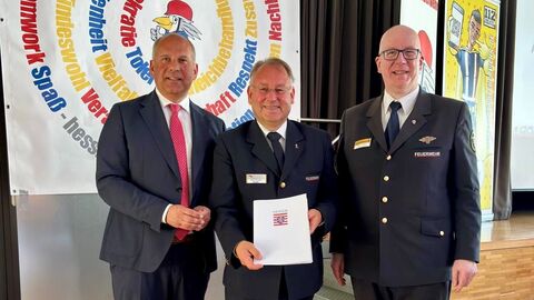 Innenminister Roman Poseck steht mit dem Präsidenten des Landesfeuerwehrverbandes Hessen Norbert Fischer und Landesjugendfeuerwehrwart Markus Potthof vor Wand mit buntem Kreis
