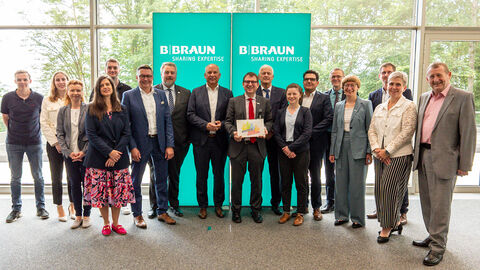 Auszeichnung für Firma B. Braun  Innenminister Roman Poseck, B. Braun-Vorstandsmitglied Dr. Stefan Ruppert, Nordhessens Polizeipräsident Konrad Stelzenbach und Landtagsabgeordneter Günther Rudolph sowie weitere Mitarbeiterinnen und Mitarbeiter der Firma B. Braun stehen zusammen vor grünem Auftseller