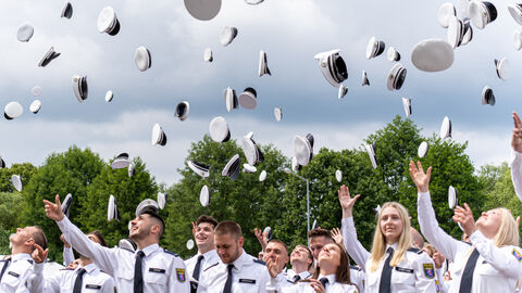 Polizisten und Polizistinnen schmeißen Mützen in die Höhe