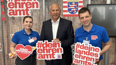 Innenminister Roman Poseck beim Stand #deinehrenamt auf dem Hessentag. Neben ihm stehen eine Frau und ein Mann, die Plakate in der Hand halten Innenminister Roman Poseck beim Stand #deinehrenamt auf dem Hessentag. Neben ihm stehen eine Frau und ein Mann, die Plakate in der Hand halten