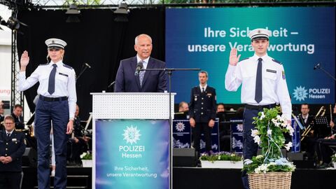Innenminister Roman Poseck bei der Vereidigung der neuen Polizeikommisaranwärter Innenminister Roman Poseck bei der Vereidigung der neuen Polizeikommissaranwärter. Er steht auf der Bühne hinter einem Pult und neben ihm zwei Anwärterinnen und Anwärter.