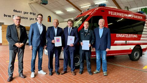Innenminister Poseck und weitere Personen stehen in einer Halle, im Hintergrund ein Feuerwehrfahrzeug.
