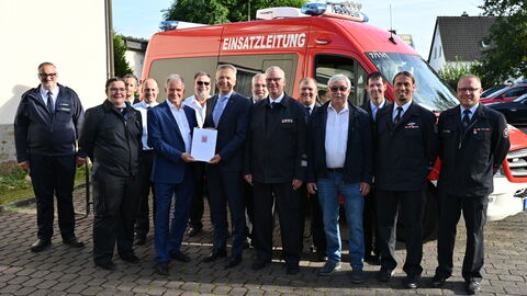 Staatssekretär Rößler steht mit Beteiligten der Frewilligen Feuerwehr Kölschhausen zusammen vor einem Feuerwehrfahrzeug.