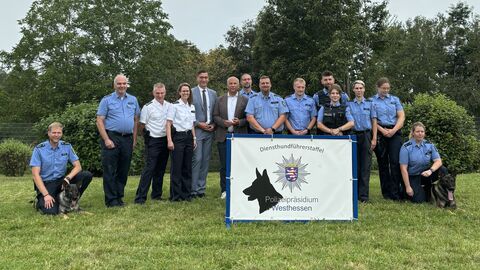 Innenminister Poseck steht mit Beamtinnen und Beamten der Diensthundführerstaffel zusammen, vor Ihnen ein Schild mit der Aufschrift "Diensthundführerstaffel Polizeipräsidium Westhessen"