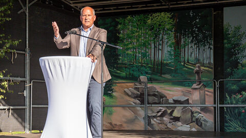 Innenminister Roman Poseck steht auf Bühne an einen weißen Tisch gelehnt. 