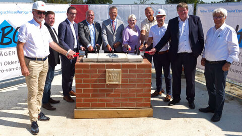 Staatssekretär Rößler steht mit weiteren Personen um einen Block Ziegel mit der Aufschrift "2024". Alle halten Hämmer in der Hand und diese liegen auf den Steinen auf.