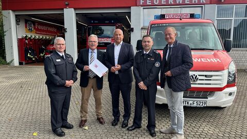 5 Männer stehen vor einem Feuerwehrhaus.