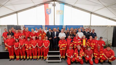 oman Poseck steht gemeinsam mit Vertreterinnen und Vertretern des Brand-und Katastrophenschutzes auf Bühne in Zelt