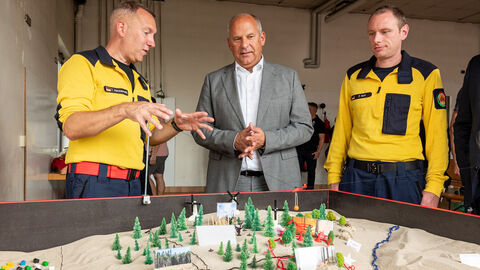 Innenminister Poseck steht mit zwei Mitgliedern der Fachgruppe für Wald- und Vegetationsbrand der Feuerwehr Fernwald im Landkreises Gießen vor Modell
