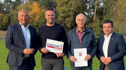 Vier Männer stehen auf einer Wiese. Einer hält einen Zuwendungsbescheid in der Hand.
