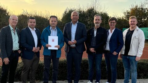 7 Personen stehen nebeneinander und lachen in die Kamera. Einer hält den Bescheid in der Hand.