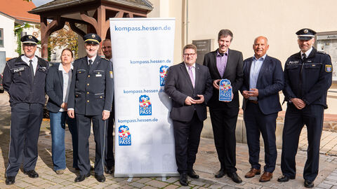 KOMPASS-Begrüßung der Gemeinde Lahnau  Mehrere Männer, teilweise in Polizei-Uniform stehen um einen Aufsteller mit dem einem Loo auf dem "Kompass" steht