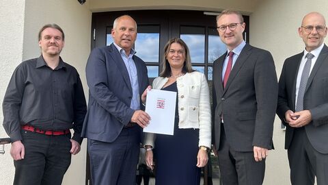 Innenminister bei Bescheidübergabe Vier Männer und eine Frau stehen vor Tür. Ein Mann hält eine weiße Mappe mit dem Hessenwappen in der Hand.