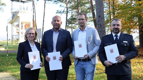 Drei Männer und eine Frau stehen auf einem Weg vor einer Wiese und halten jeweils eine Absichtserklärung über eine Kooperation in der Hand.