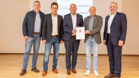Kommunalminister Poseck steht mit weiteren Personen zusammen und überreicht dem Siegbacher Bürgermeister Maik Trumpfheller den IKZ-Förderbescheid.