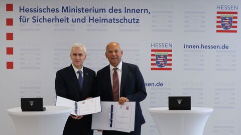 Zwei Männer stehen nebeneinander und halten die unterzeichneten Absichtserklärung hoch.