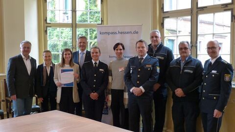 Einige Frauen und Männer in Polizeiuniform stehen vor einem Plakat. Darauf steht: kompass.hessen.de
