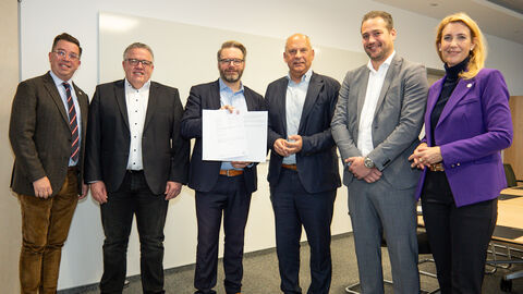 Fünf Männer und eine Frau stehen nebeneinander. Der Mann in der Mitte hält eine Urkunde hoch.