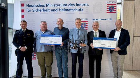 Mehre Männer stehen vor einem große Aufsteller des Hessichen Innenministeriums. Einige halten Schilder mit der Fördersumme