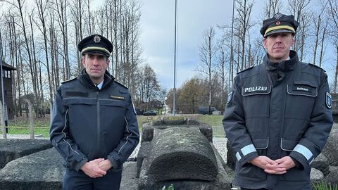 Zwei Männer stehen rechts und links neben einem niedergelegten Kranz.