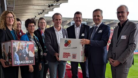 Acht Personen stehen im Sitzbereich eines Stadions.