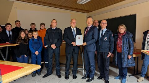 Staatssekretär Rößler steht mit weiteren Personen in einem Raum und überreicht einen Förderbescheid.