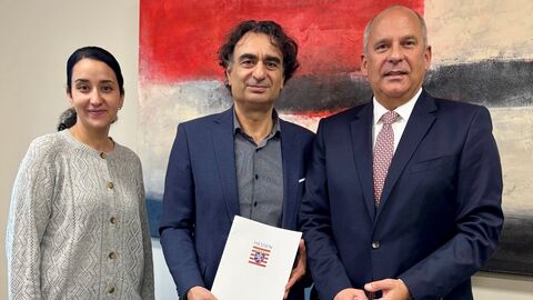 Innenminister Poseck steht mit zwei Personen nebeneinander. Ein Mann in der Mitte hält einen Förderbescheid in Händen.