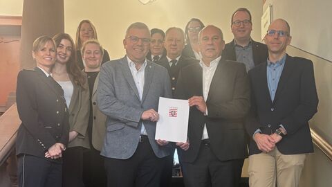 Mehrere Menschen stehen auf Treppe und lachen in Kamera. Zwei halten Förderbescheid.