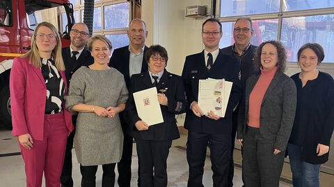 9 Personen stehen nebeneinander in einem Feuerwehrhaus.