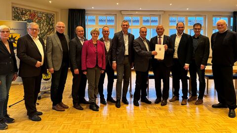 Eine Gruppe Personen steht zum Gruppenfoto aufgestellt in einem Raum.