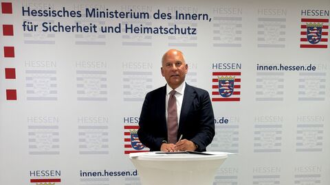 Roman Poseck bei Unterzeichnung der Kooperationsvereinbarung Mann steht vor einem Plakat