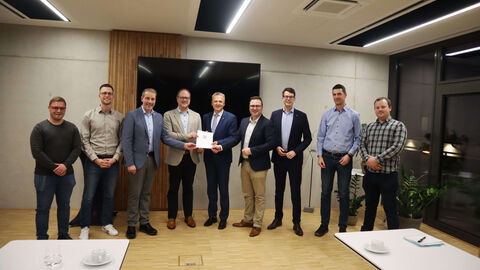 Innenstaatssekretär Martin Rößler steht mit weiteren Personen zum Gruppenfoto aufgestellt in einem Raum. Er überreicht einen Bescheid.