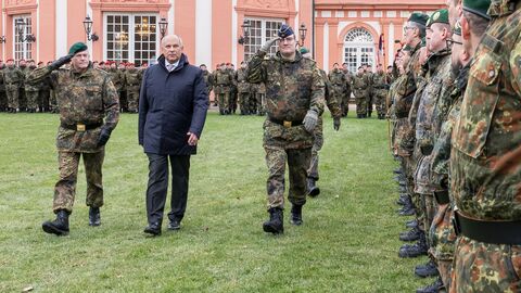Roman Poseck läuft über eine Wiese, im Hintergrund salutieren Beamte der Bundeswehr und man sieht das Schloss Biebrich