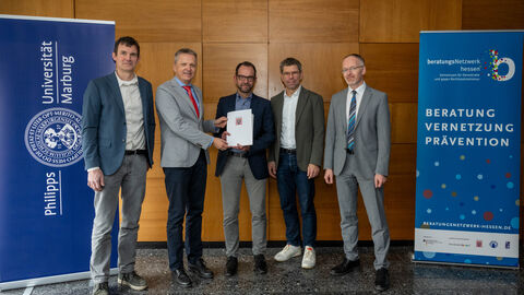 Fünf Männer stehen nebeneinander und halten einen Förderbescheid in der Hand.