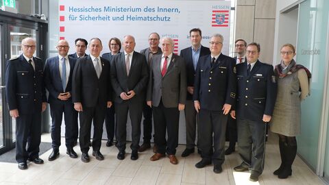 Innenminister Roman Poseck steht mit dem Präsidenten der IGMK, Herrn Dietmar Jerger, Vertretern der Karnevalsvereine, des HMdI und der Polizei in einem Raum zum Gruppenfoto aufgestellt.
